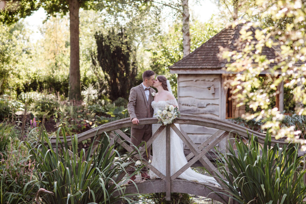 Bride and Groom share a kiss on bridge at countryside wedding venue on a sun filled day