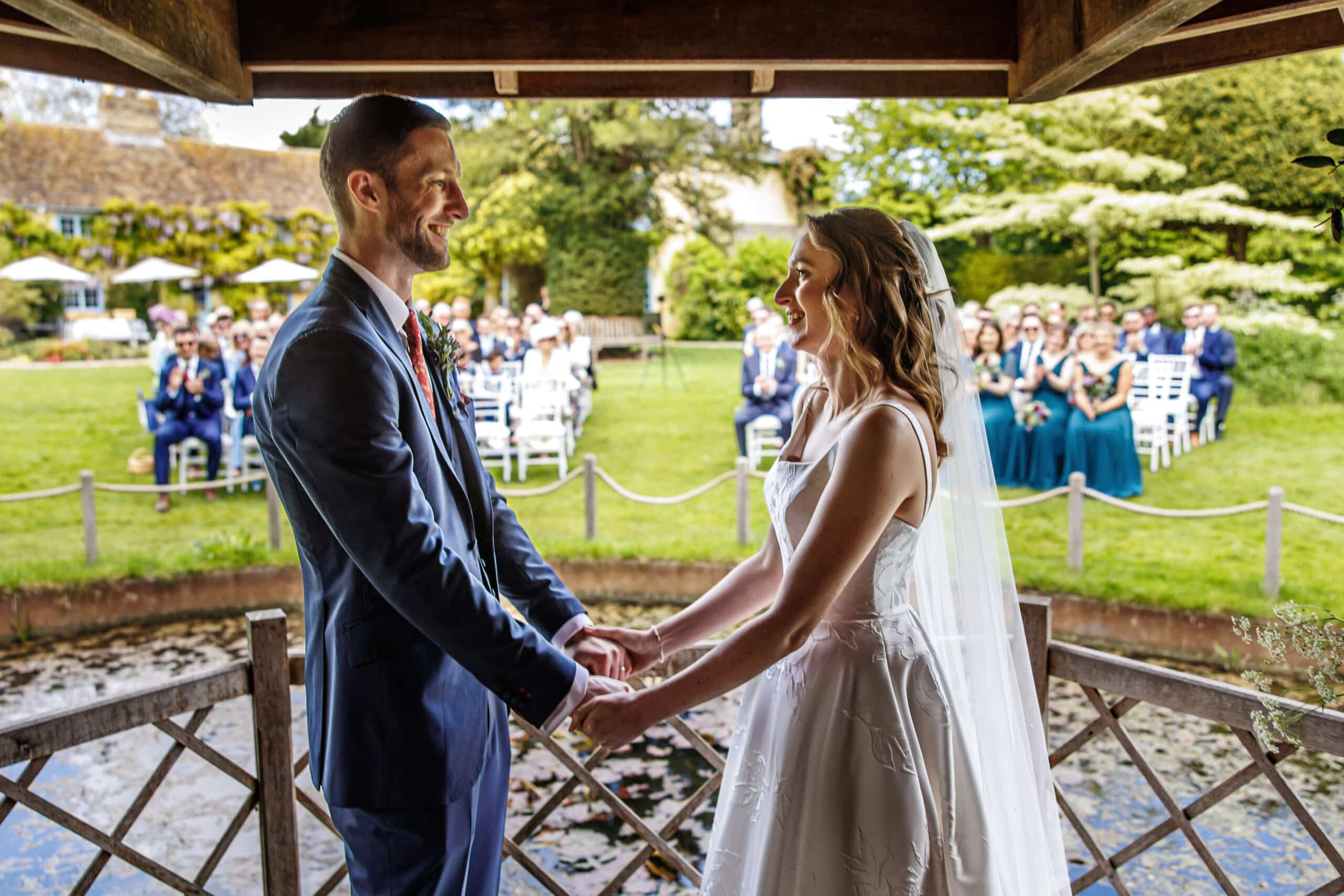 Bride and groom hold hands during garden wedding ceremony with guests watching on