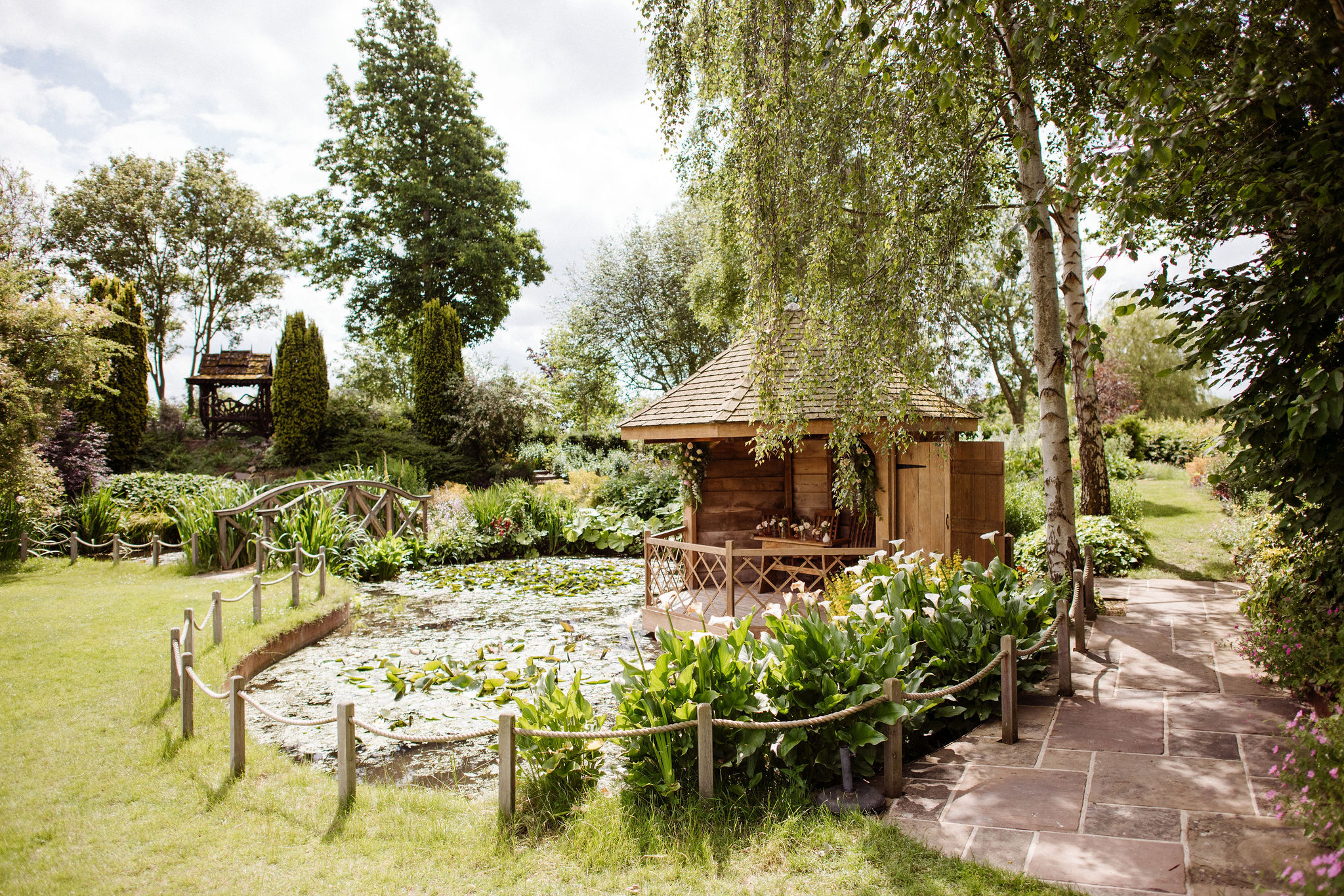 Pretty summerhouse next to lilly pad filled pond with stunning gardens in the background at countryside wedding venue