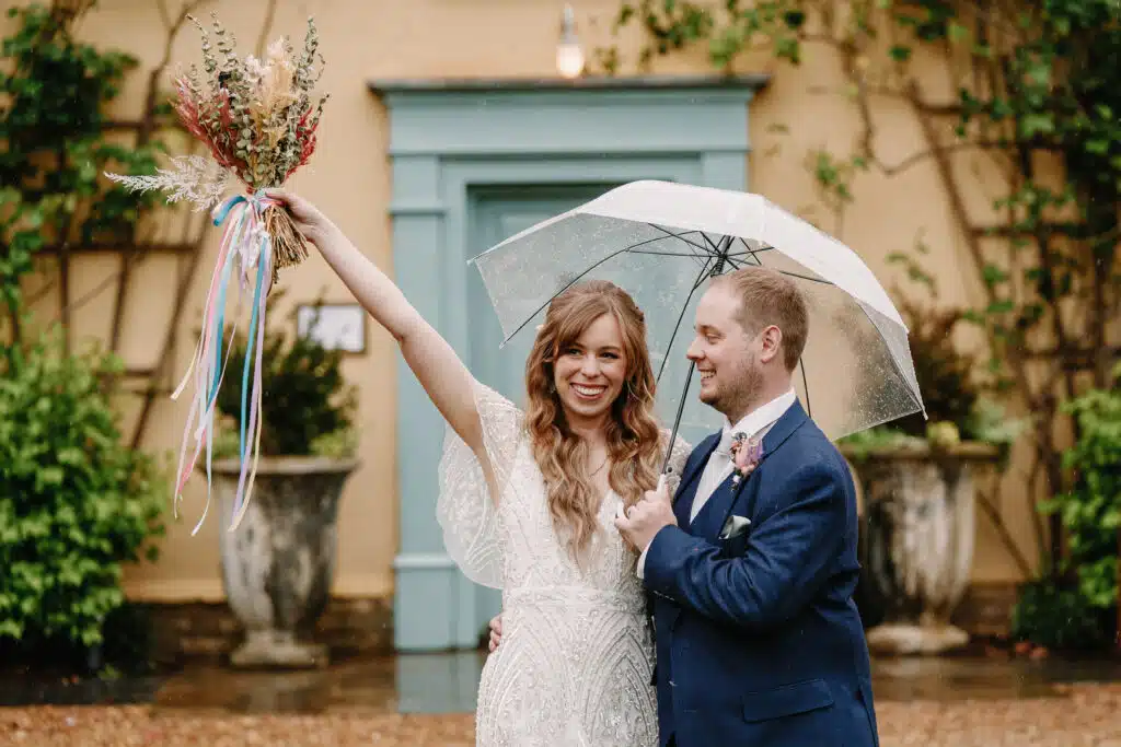 Bride and Groom under umbrella standing at the front of South Farm's Farmhouse