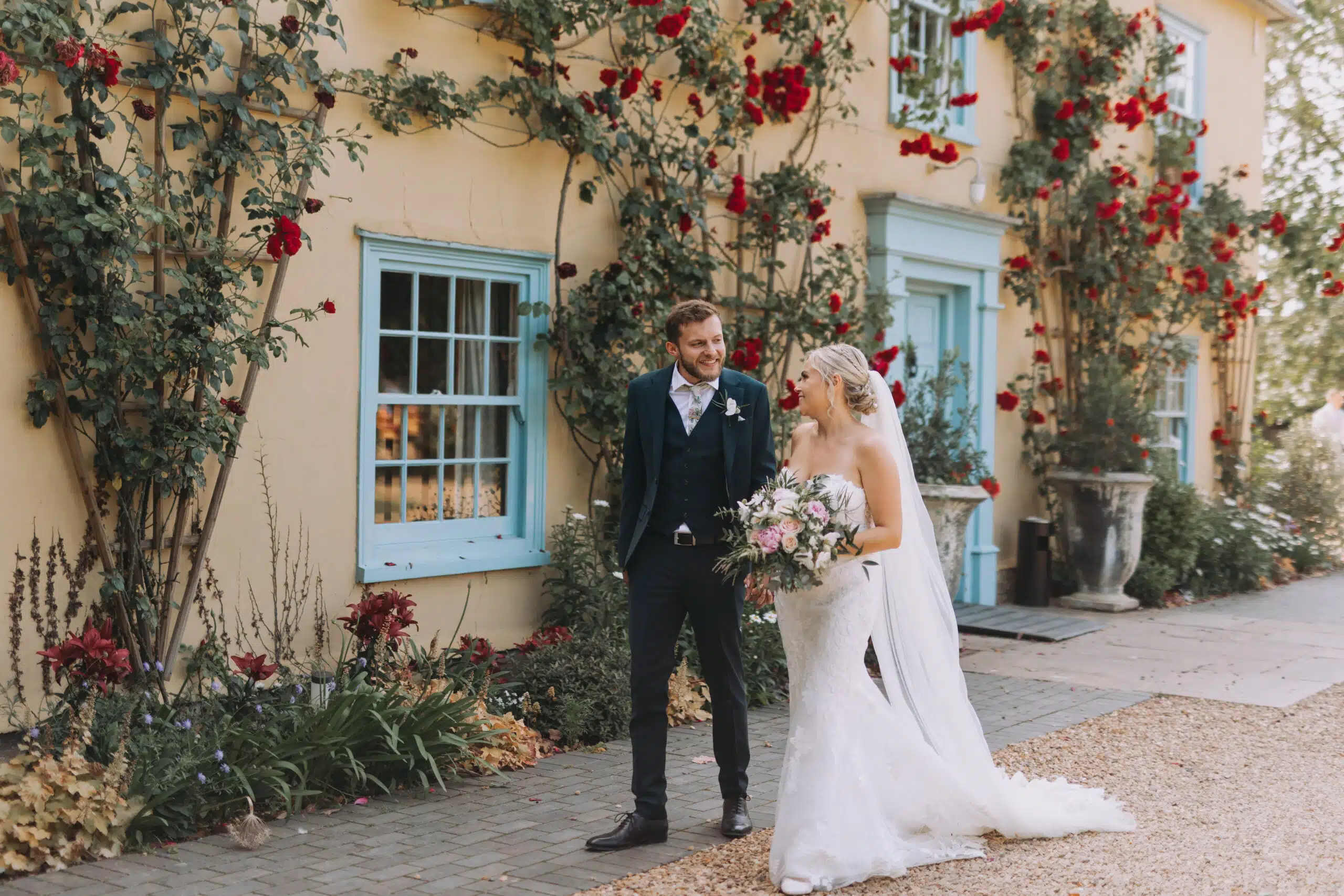 Bride and Groom walking in front of the charming country farmhouse adorned with red roses