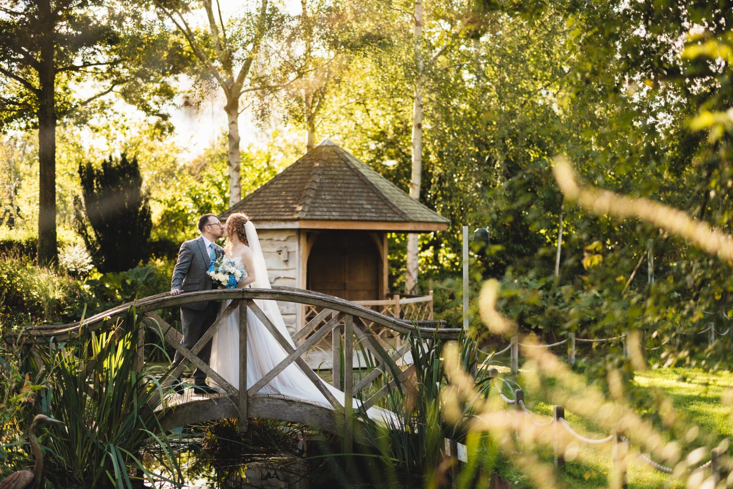 Bride and Groom on the Monet Bridge with the Summer House behind them at outdoor countryside wedding venue
