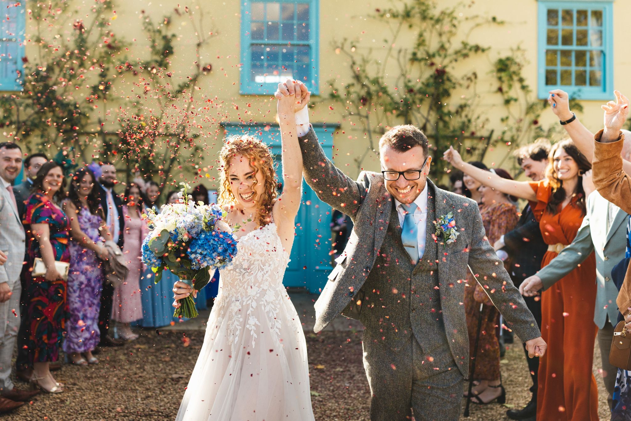 Bride and groom hands in air enjoying their confetti exit in front of the charming farmhouse at South Farm 