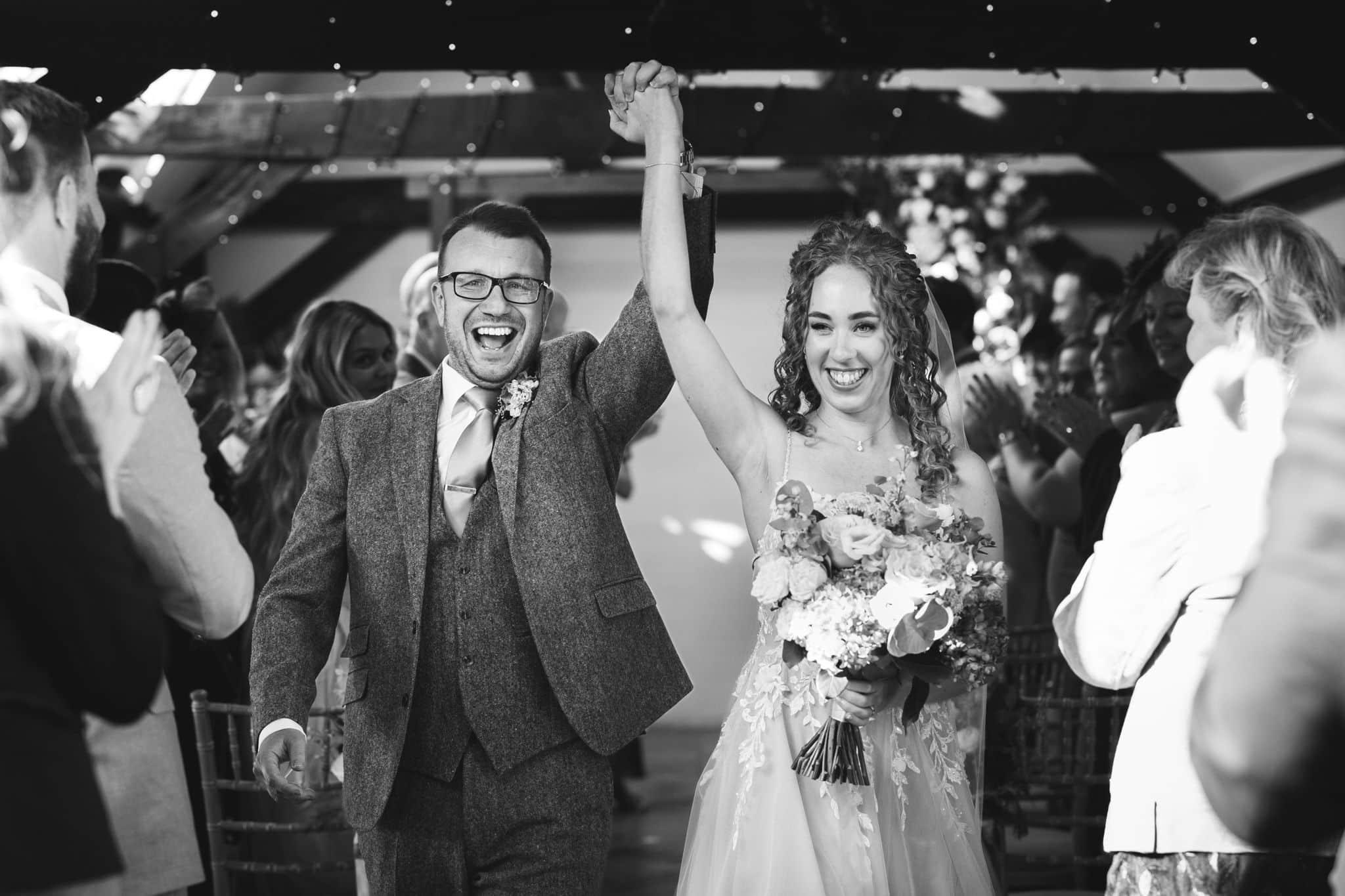 Bride and Groom hands in air in the rustic Old Dairy after saying I Do at Countryside wedding venue 