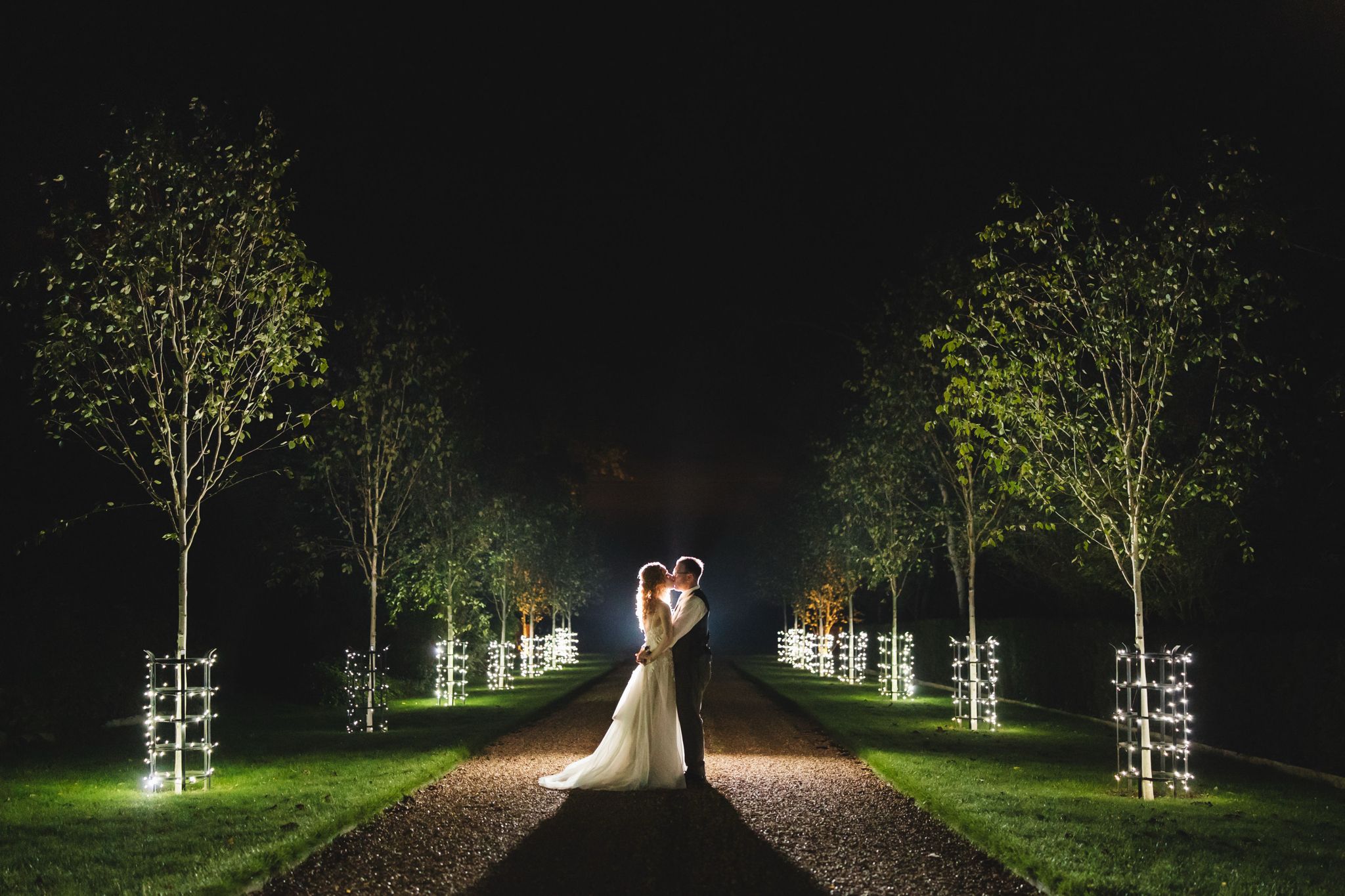 Bride and Groom at twilight having a kiss on the fairy-lit driveway at Barn wedding venue in Hertfordshire