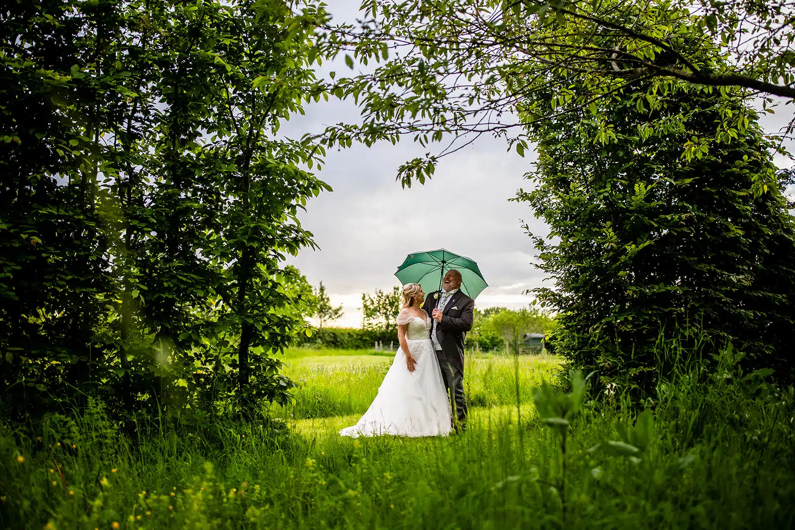 Bride and Groom in the Arboretum under an umbrella at South Farm wedding venue