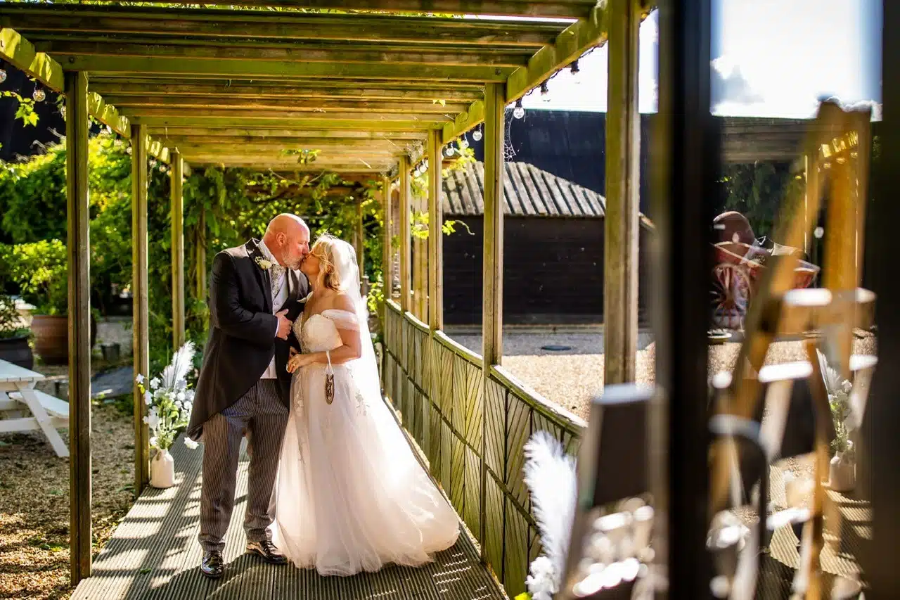 Bride and Groom stood on the walkway leading to the Tudor Barn adorned with fairy lights ready to have their wedding breakfast and Farmyard with piglets in view