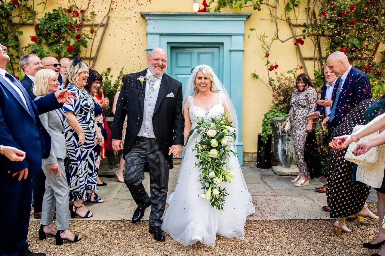 Bride and Groom enjoying a confetti exit in front of iconic blue door at South Farm wedding venue based in Hertfordshire