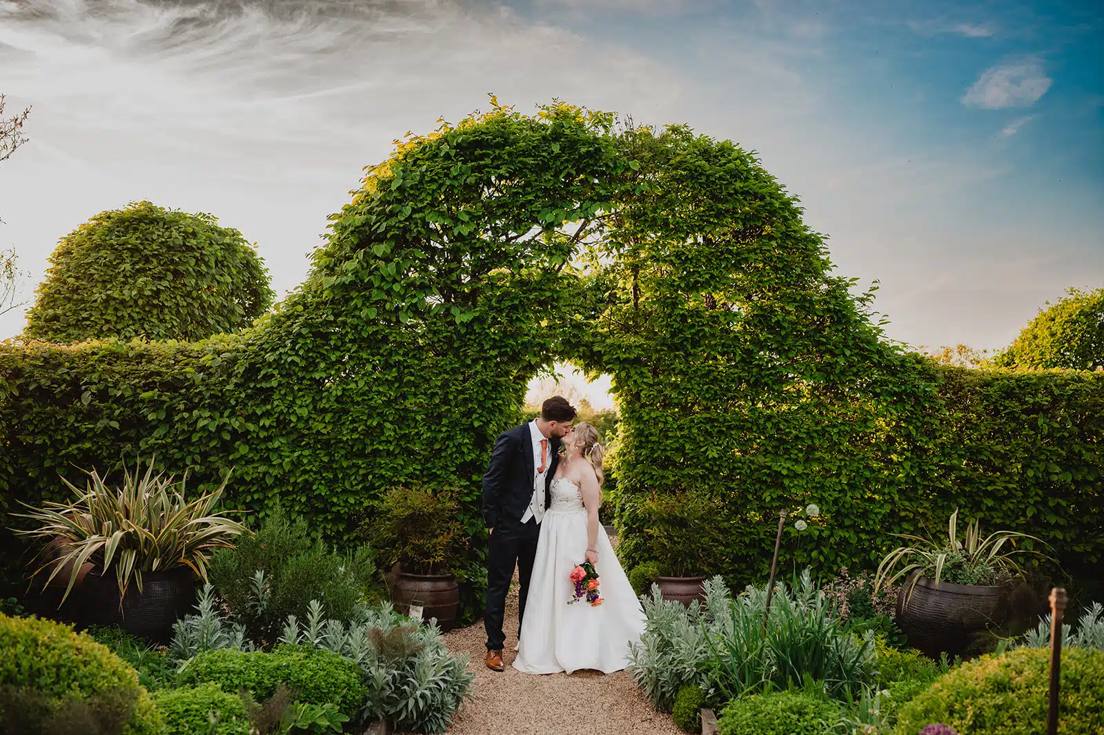 Bride and Groom in the Kitchen Garden with hedges behind them at Golden Hour at eco friendly wedding venue