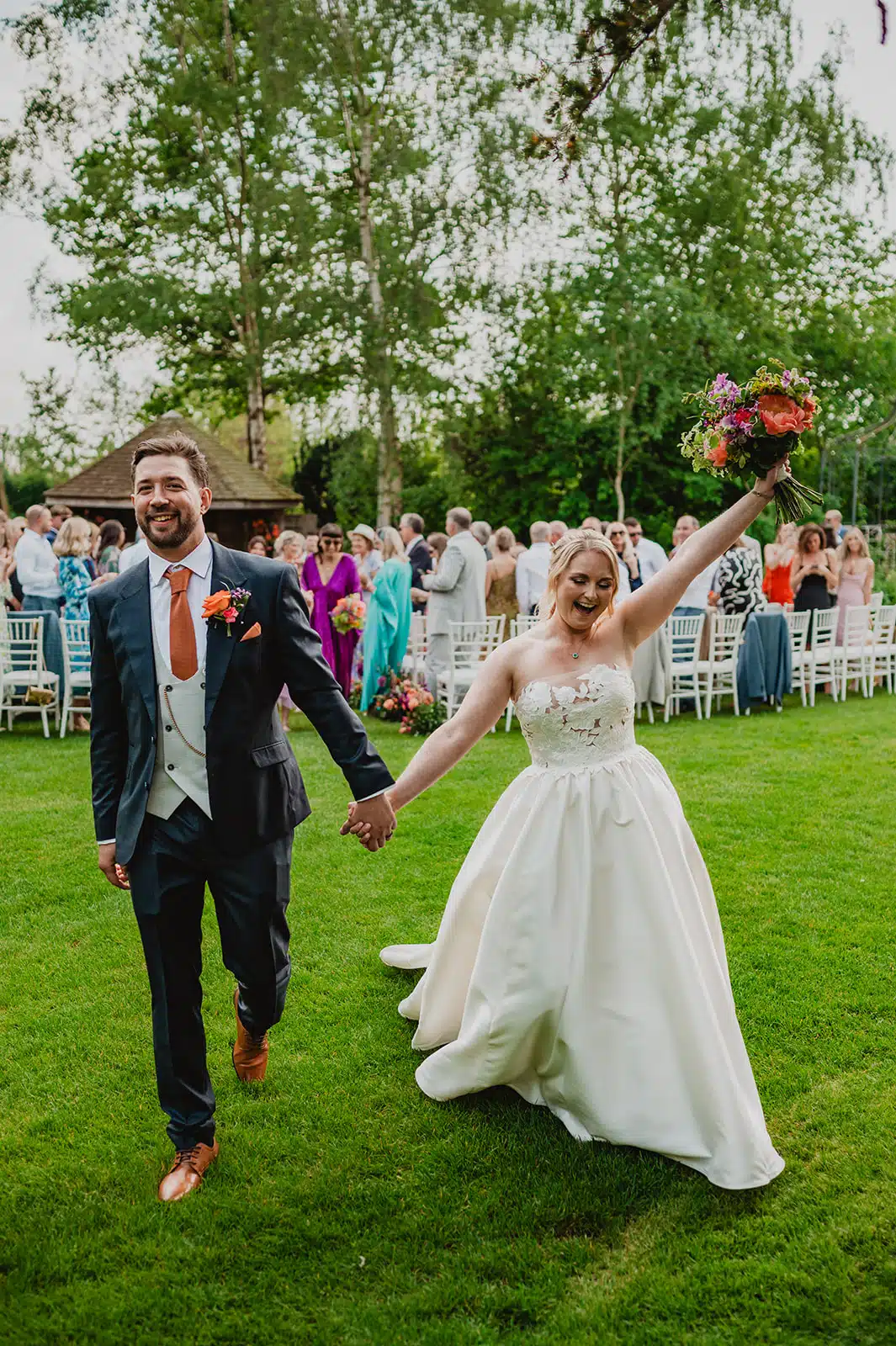 Bride and Groom with hands in the air walking up the aisle after saying their 'I dos' in the outdoor Summer House at South farm