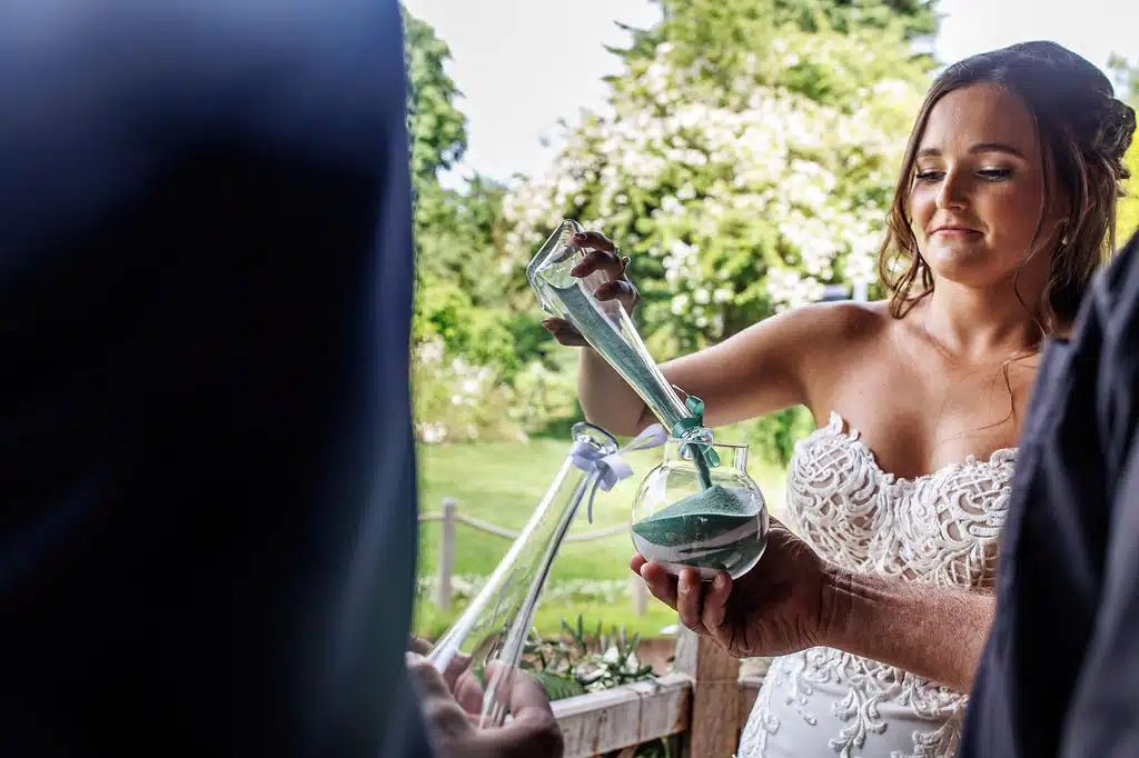 Bride pouring sand into glass bottles part of their humanist ceremony at barn wedding venue in Hertfordshire