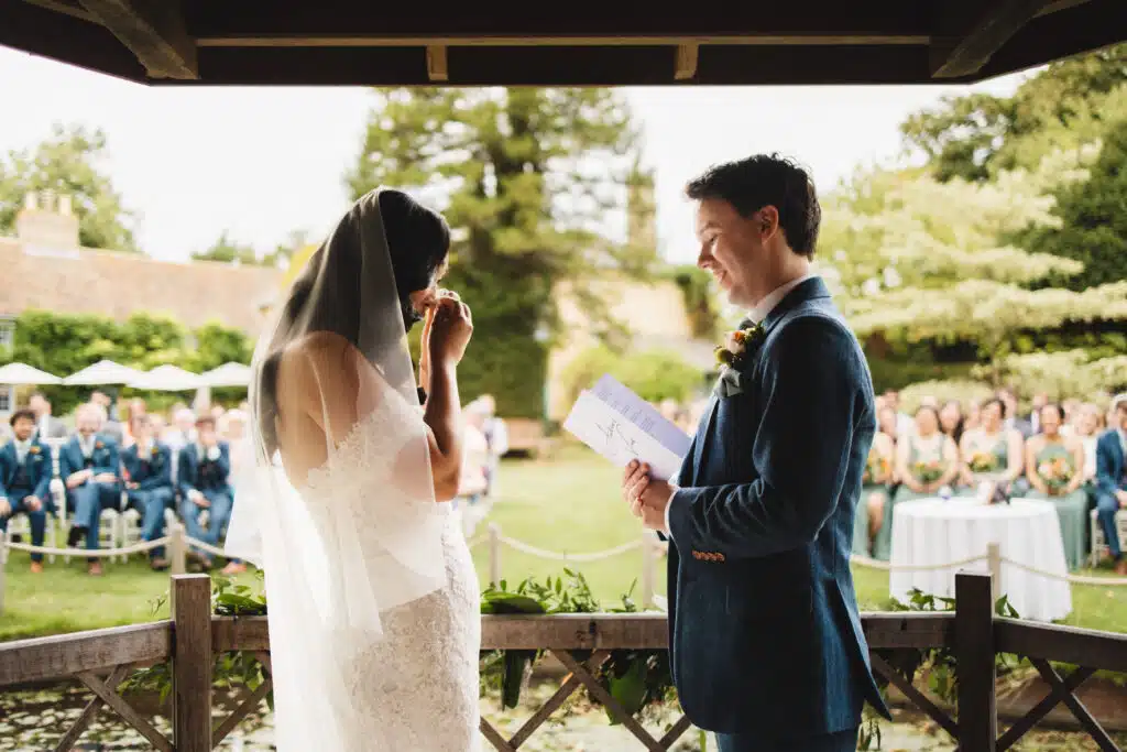 Bride and Groom stand in the Summerhouse with their guests watching as they listen to the groom saying his vowels. Emotional bride wiping away her tears of happiness.