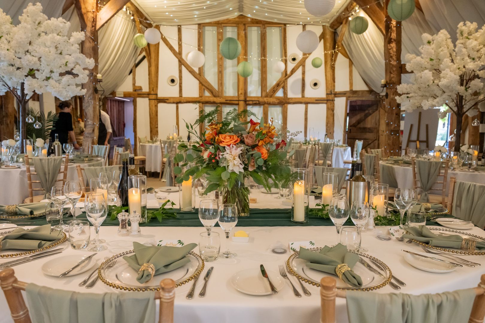 Sage green and orange florals on the tables in the Tudor Barn with led candles lit adding to the ambiance