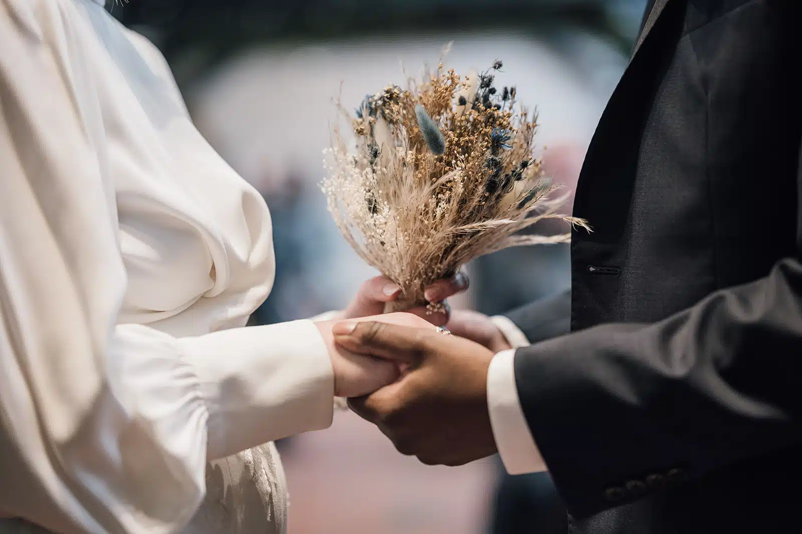 Bride and Groom hold hands during their ceremony in the Old Dairy. Bride holds her dried floral boquet.