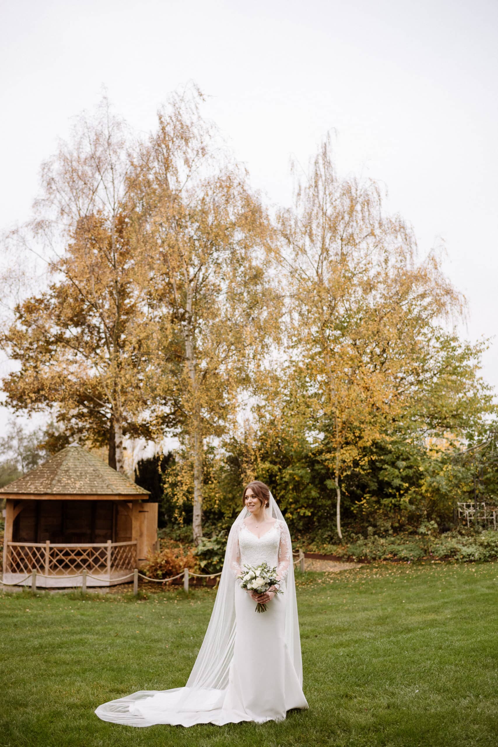 Bride standing on the lawn in front of the Summerhouse with very autumnal backdrop at garden wedding venue