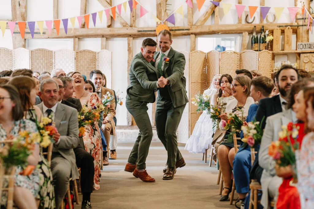 The Groomsmen dancing down the aisle at indoor ceremony in the Tudor Barn at barn wedding venue in Hertfordshire