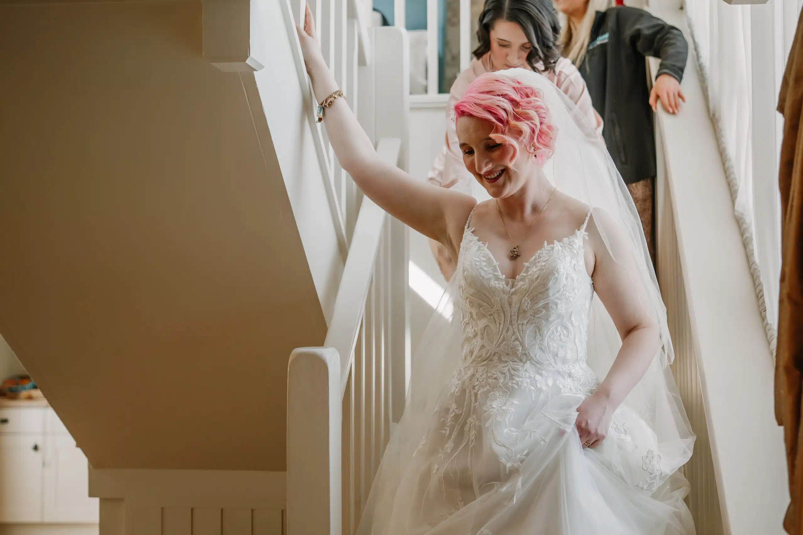 The bride with bright pink hair walking down the stairs ready for the ceremony to take place in the Tudor Barn at barn wedding near Bedfordshire