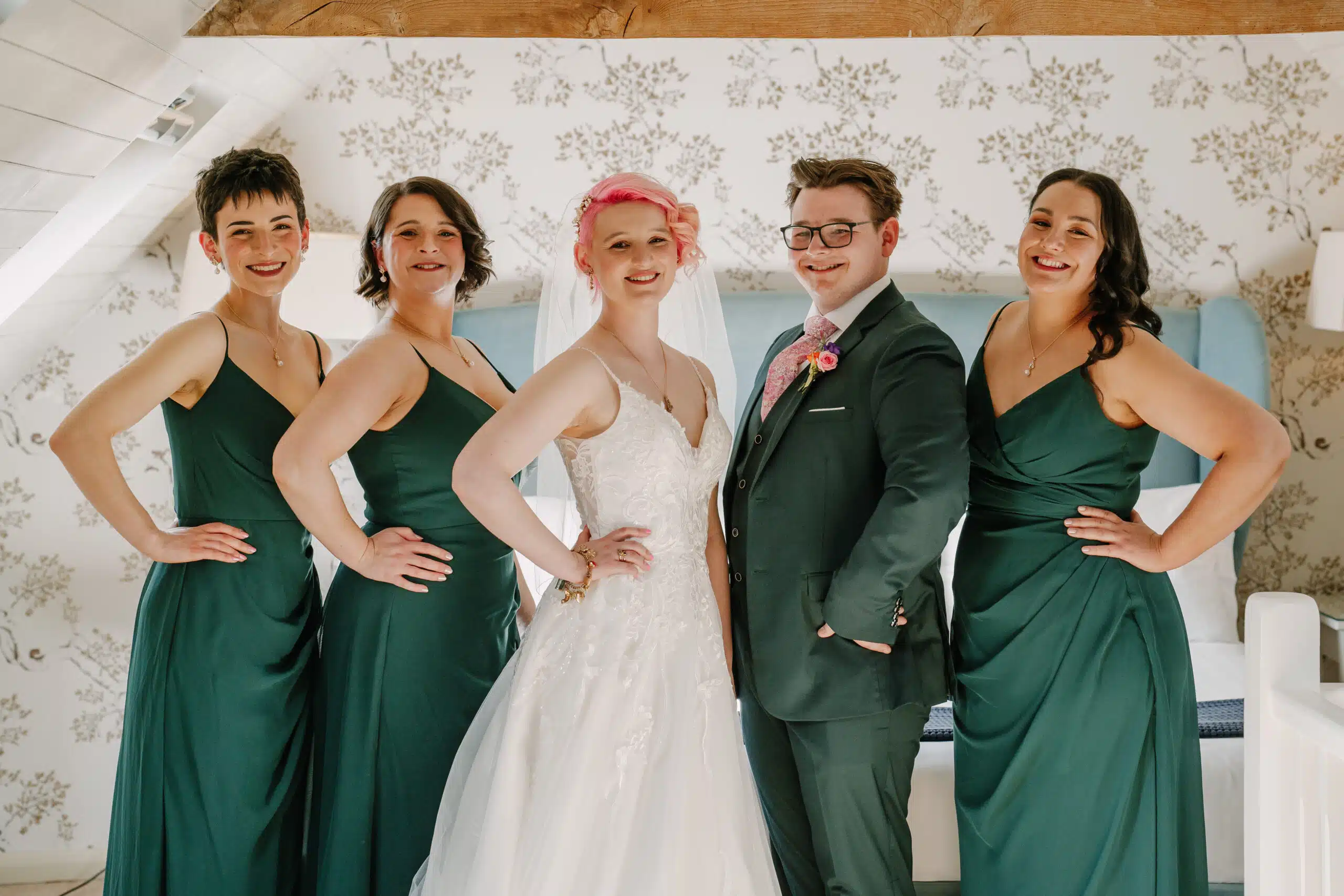 The bride with bright pink hair and her bridal party standing in The Coach House Suite at barn wedding venue in Cambridgshire 
