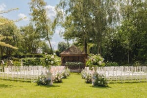 Wedding ceremony set up in stunning wedding garden at countryside wedding venue with white ceremony chairs, a pretty garden summerhouse and beautiful flower arrangements