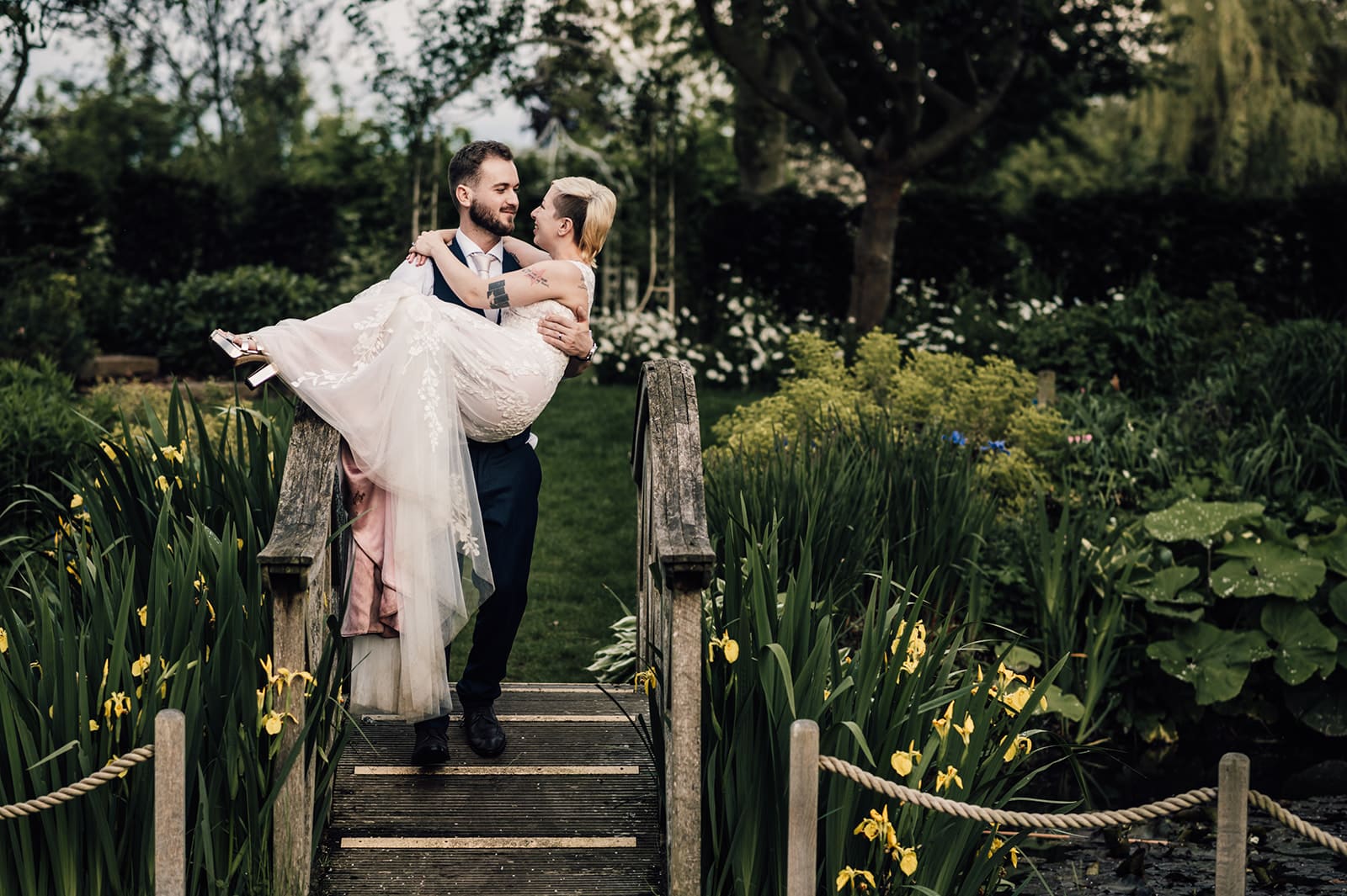 Groom holding bride on the Monet Bridge at outdoor garden wedding venue in Hertfordshire