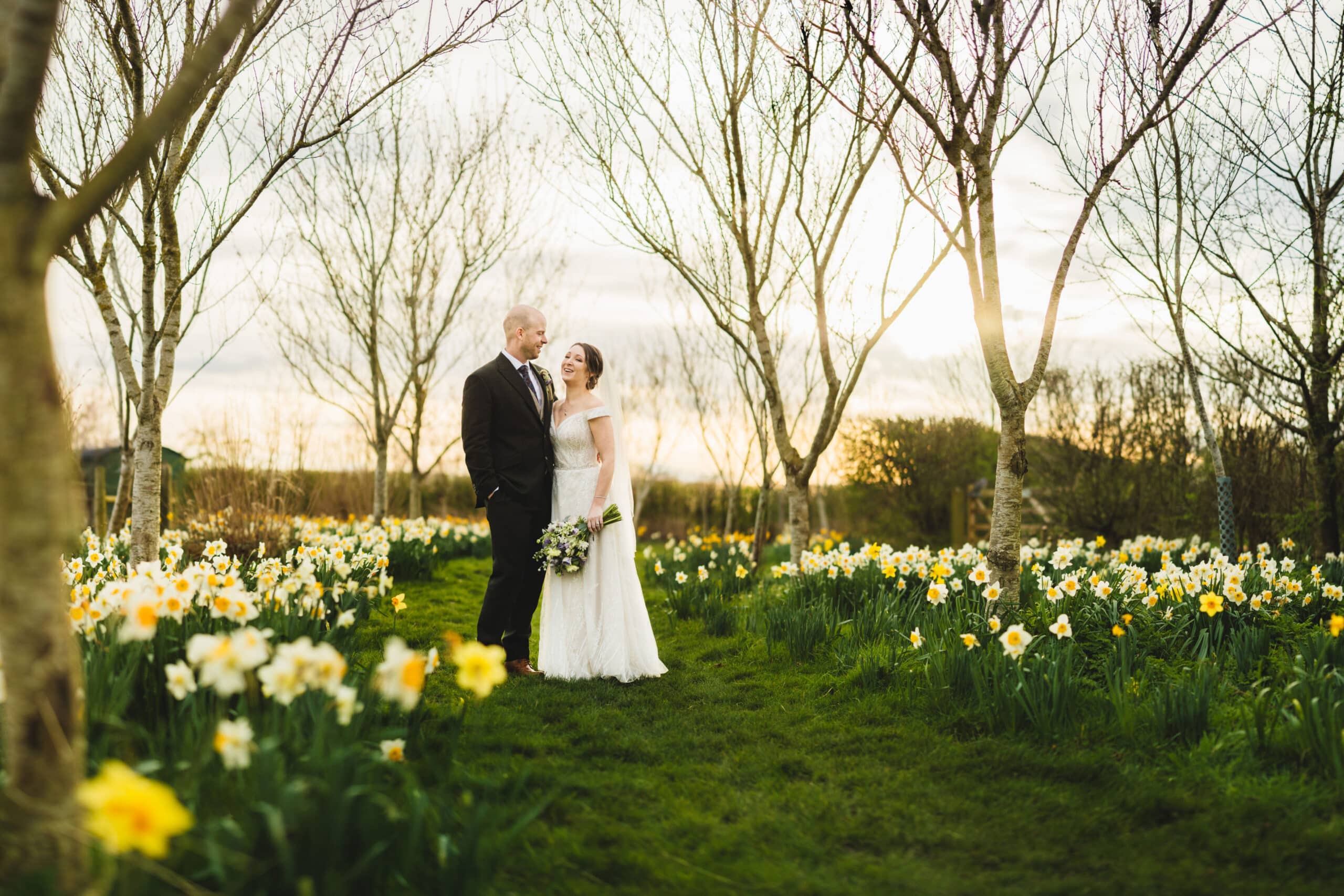 Bride and Groom standing in amongst the daffodils in meadow at outdoor garden wedding venue in Hertforshire