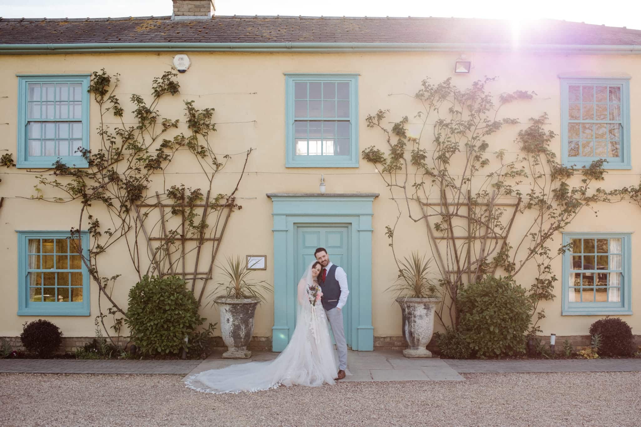 Bride and Groom standing in front of charming farmhouse with iconic blue door at countryside wedding venue in Cambridshire