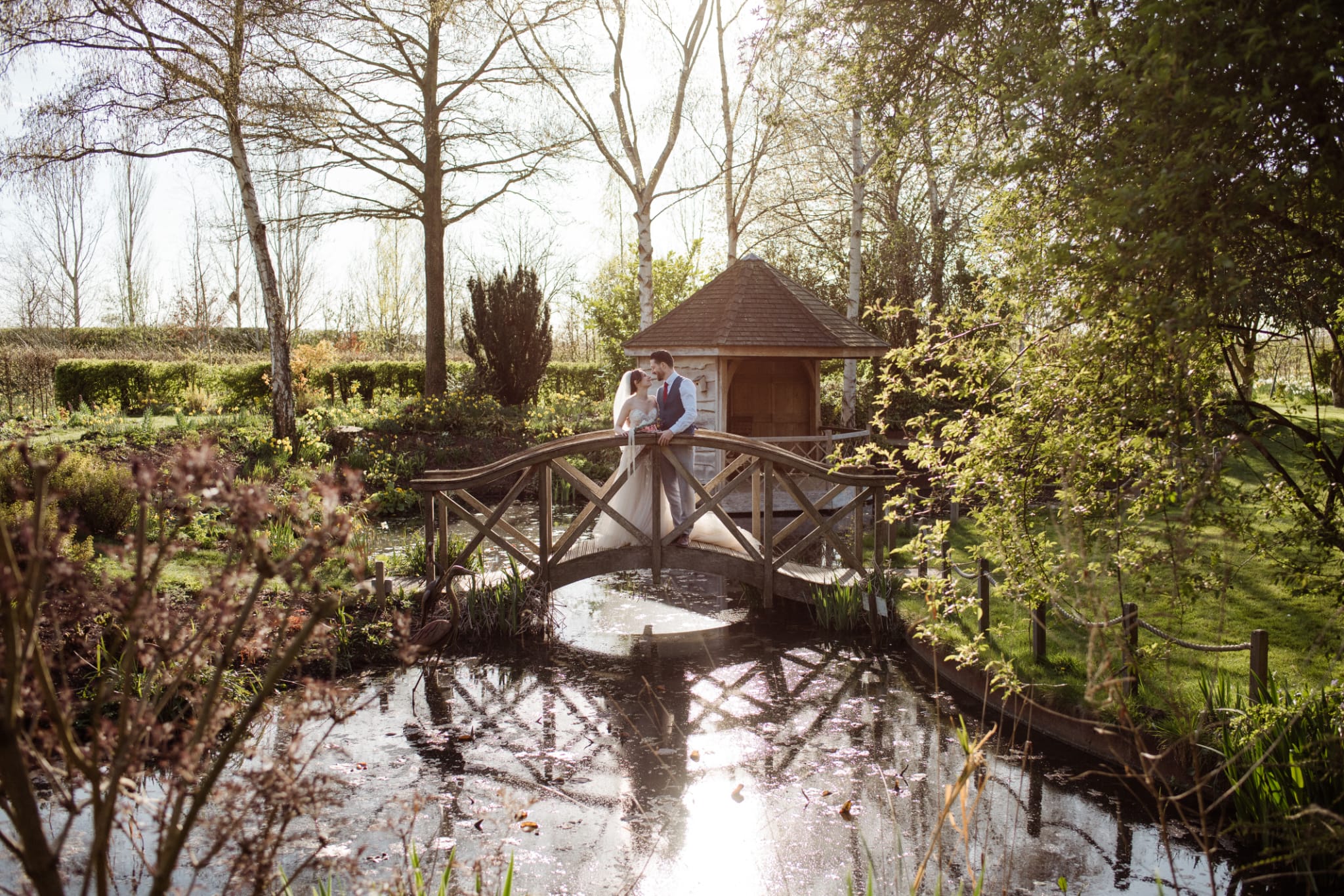 Bride and Groom standing on the Monet Bridge with stunning spring backdrop and Summerhouse behind them