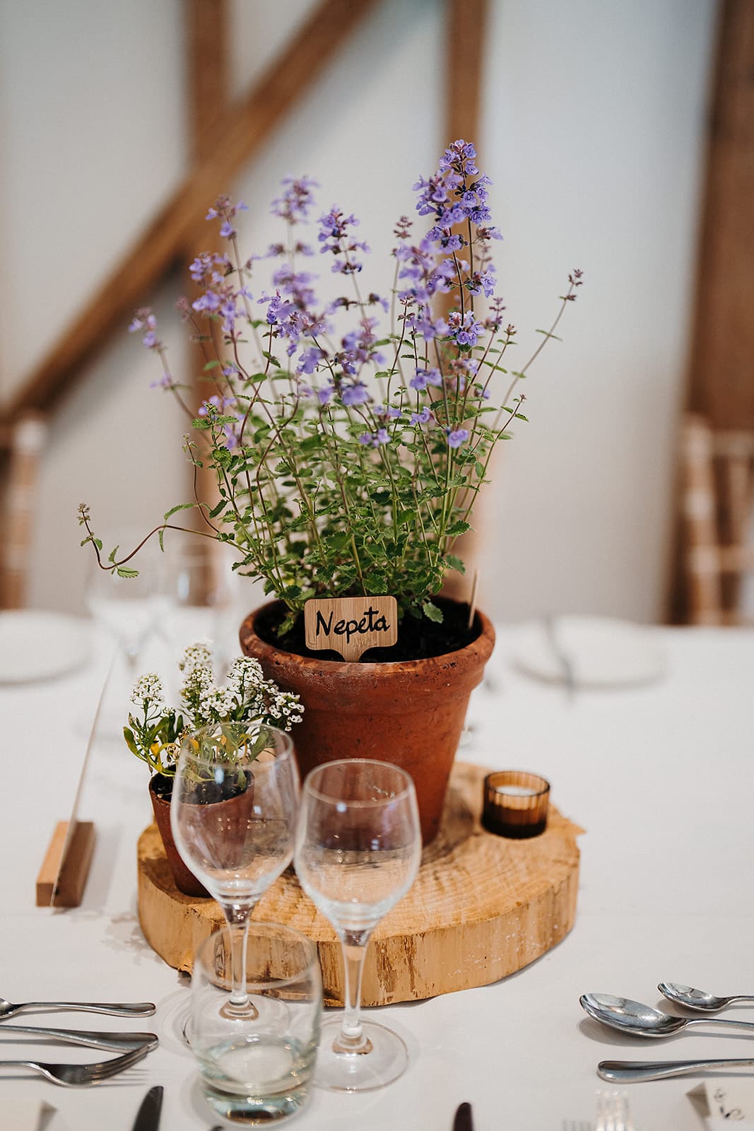 Eco table setting at wedding venue purple flowering herbs in terracotta post on natural log round