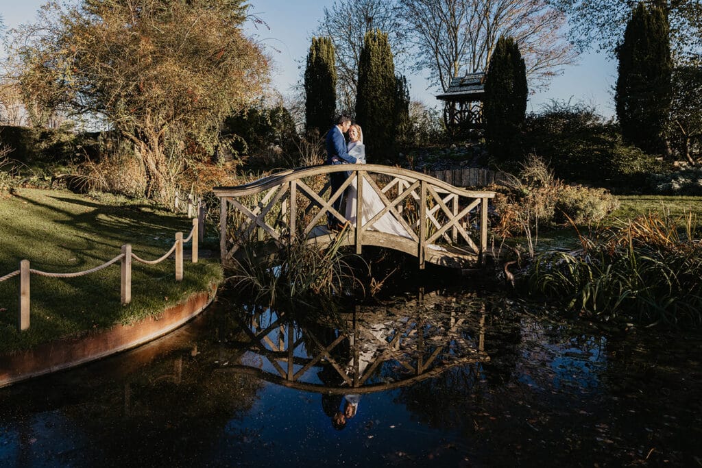 December winter wedding day at countryside farm wedding venue bride and groom on bridge over pond on sunny winter day