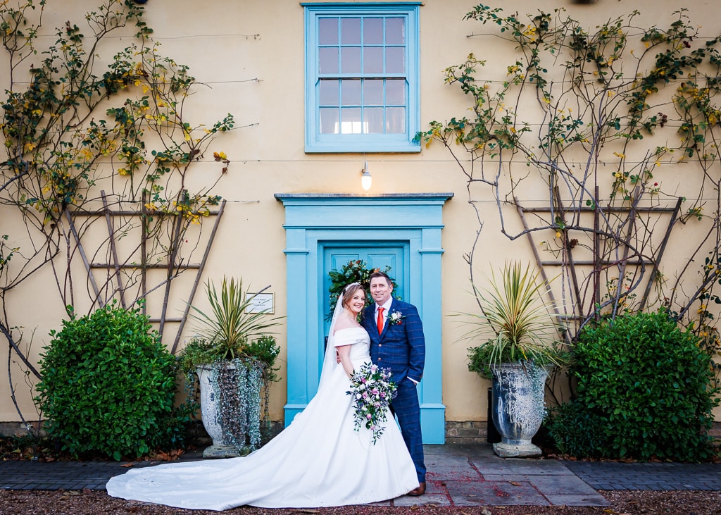 Bride and Groom standing at the front of the charming farmhouse at winter wedding venue in Cambridgeshire