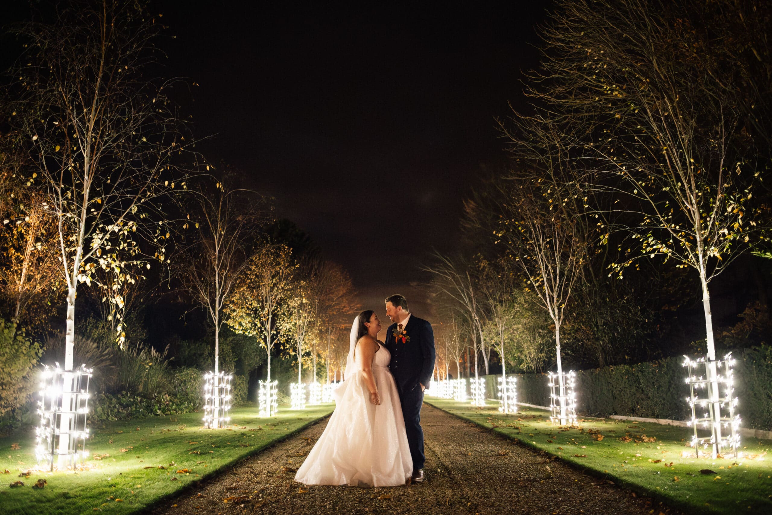 Couple embracing under illuminated trees.