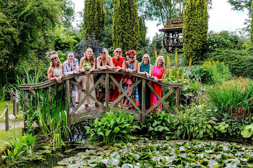 Vibrant wedding guests standing on Monet Bridge at outdoor garden wedding venue in Hertfordshire