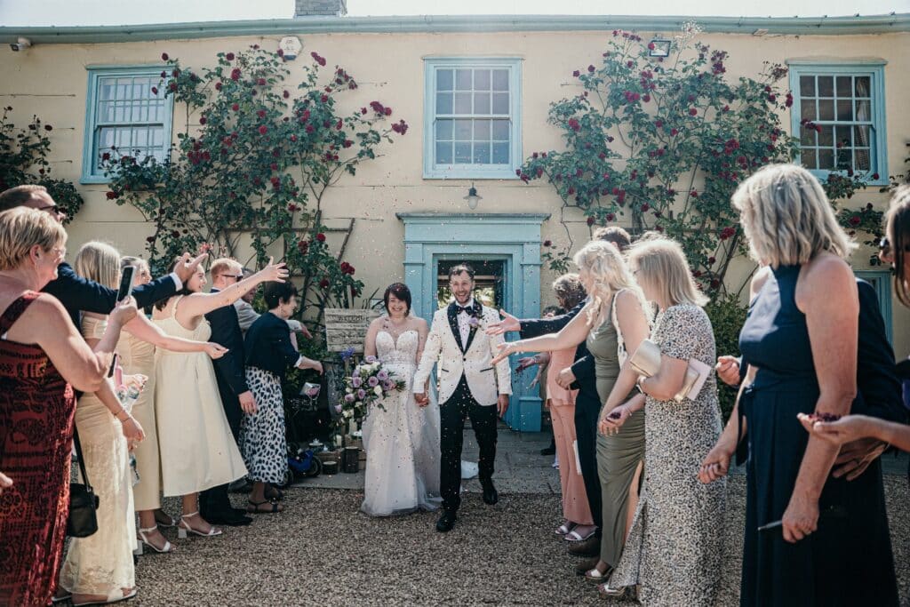 Bride and groom have confetti shower on sunny spring wedding day in front of country farmhouse