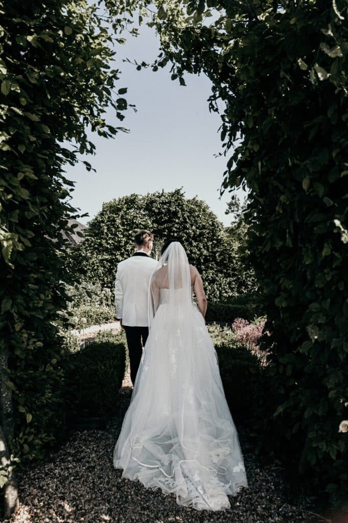 Bride and groom walk away from camera through a pretty natural hedge arch on wedding day at farm wedding veue