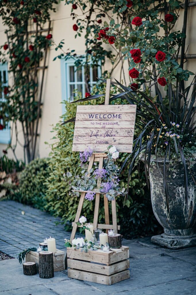 Beautiful rustic guest sign in front of country house wedding venue with red roses around the door