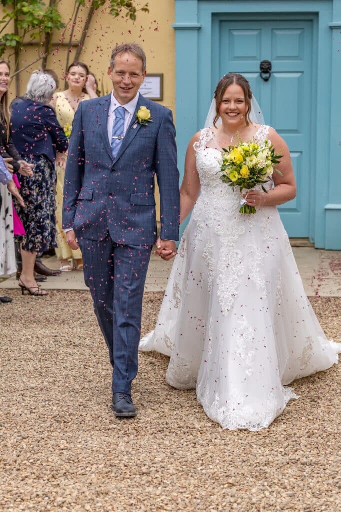 Bride and groom enjoy confetti show in front of country farm wedding venue