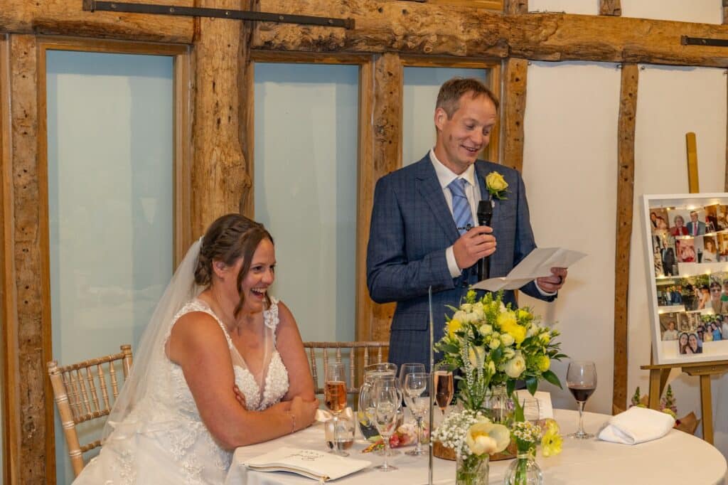 Happy bride and groom during grooms speech in stunning barn wedding venue