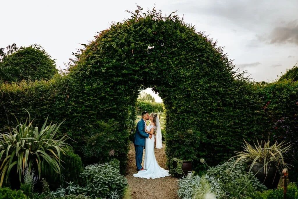 Bride and groom under natural hedge cut out arch at farm wedding venue